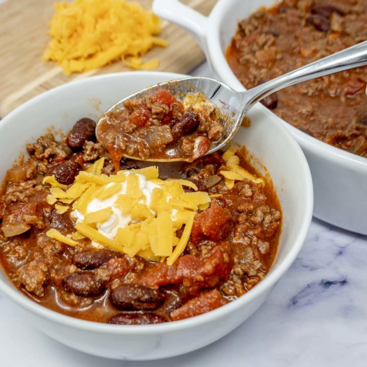 Spoon in a bowl of chili topped with cheese and sour cream