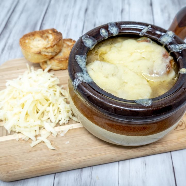 Crock of soup covered with cheese beside a pile of shredded cheese and croutons
